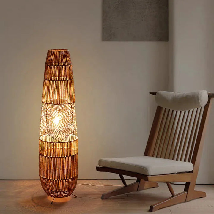 Rattan floor lamp with warm light beside a modern wooden lounge chair in a minimalist room